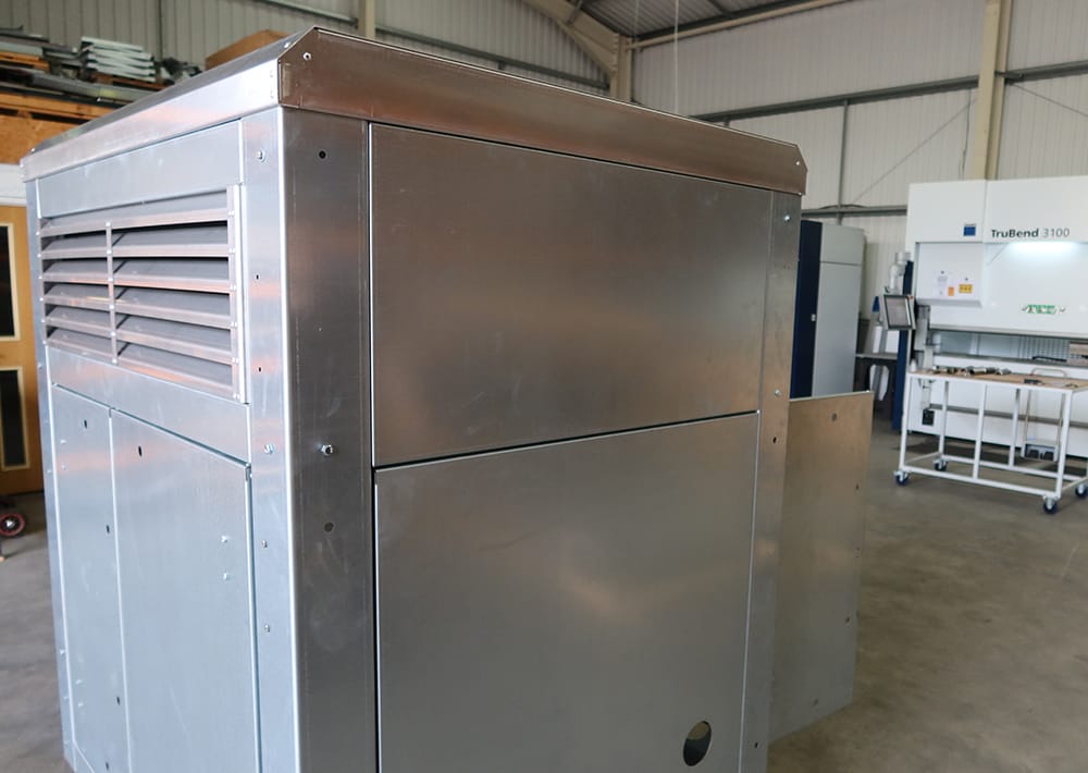 A large industrial CNC metalworking machine with ventilation slats is showcased in a warehouse, highlighting precision engineering services; additional fabrication equipment and metal parts production tools are visible in the background.