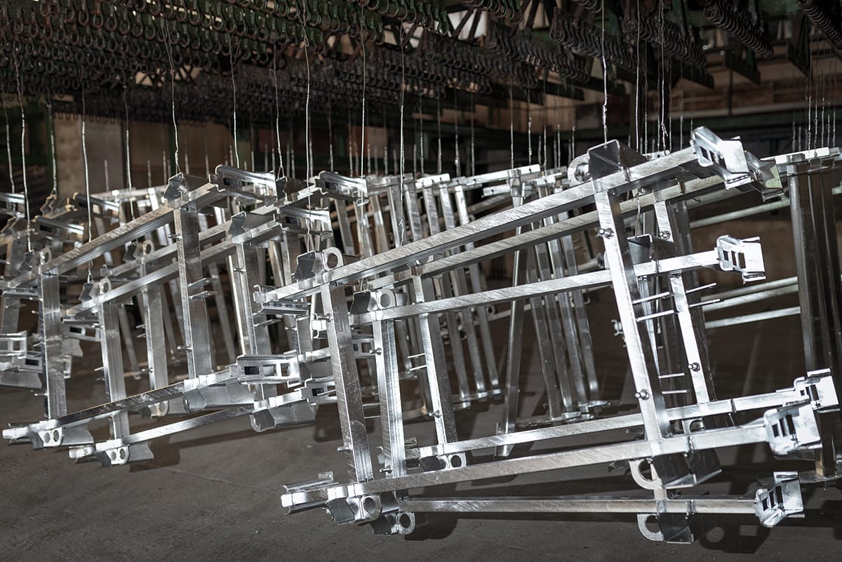 Several precision-engineered metal frames are suspended from hooks, showcasing CNC machining and metal fabrication capabilities in an industrial workshop.
